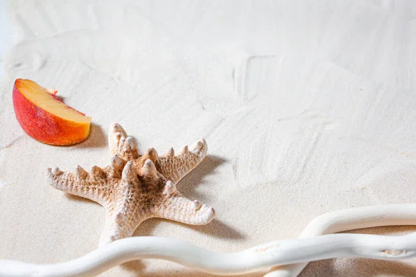 Vacaciones en playa. Las estrellas de mar, y una rama de árbol blanco y frutas jugosas se encuentran en la arena fina blanca. Fondos de escritorio . — Foto de Stock