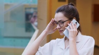 Genç iş kadını akıllı telefon kullanıyor. Beyaz tişörtlü ve gözlüklü kız bir telefon görüşmesi yaptı..