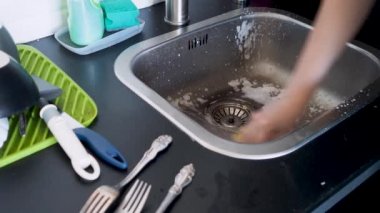 Elle bulaşık yıkayan, eldivensiz genç bir kadın bıçakları yıkıyor.