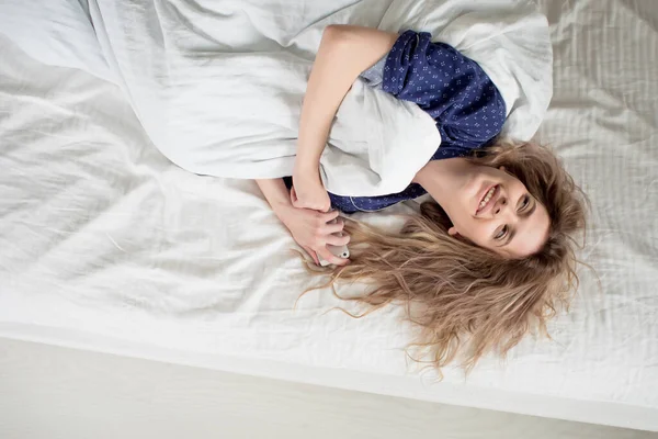 Утром женщина под одеялом выключает будильник. — стоковое фото