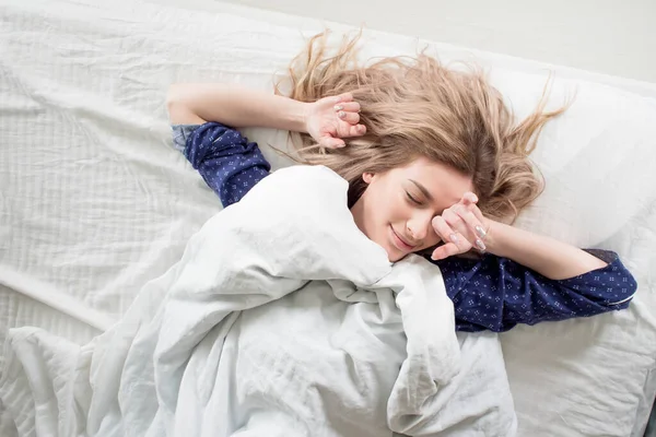 Nette Blondine in ihrem Bett im blauen Pyjama, unter einer Decke — Stockfoto