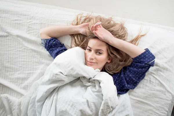 Loira bonito em sua cama em pijama azul, sob um cobertor — Fotografia de Stock