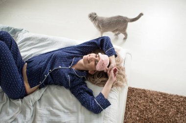 Mavi pijamaları ve uyku maskesiyle yatağında tatlı bir sarışın.,