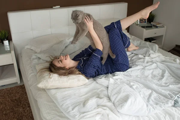 Vacker ung flicka i pyjamas kramar sin katt liggande i sängen, — Stockfoto