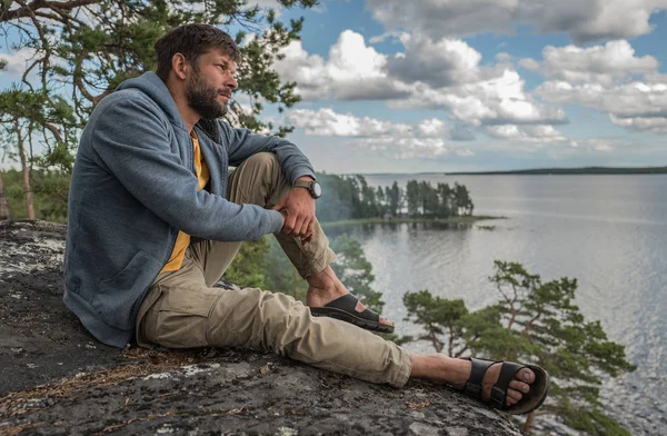 Hombre guapo está sentado en la roca y mirando a la distancia — Foto de Stock