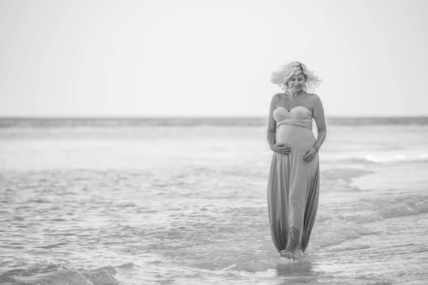 Schöne schwangere Frau hält ihren Bauch und geht auf der Sandbank — Stockfoto