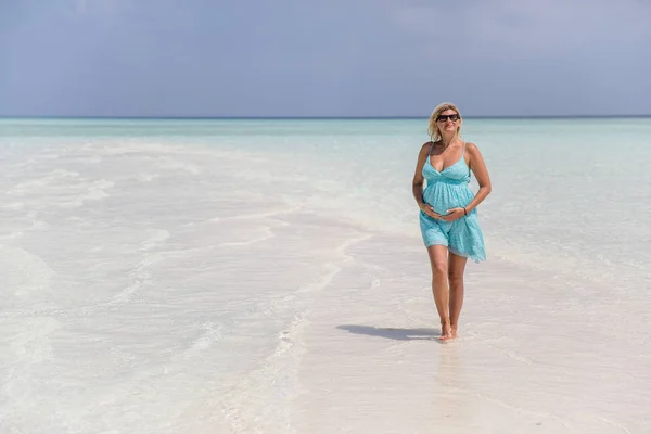 Беременная женщина держит живот и ходит по песчаному берегу — стоковое фото