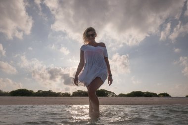 Beyaz plaj elbiseli güzel kız denizde yürüyüş