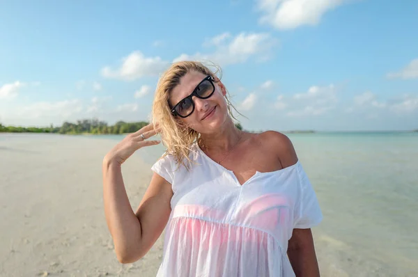 Blond flicka i vit Strandklänning ler på stranden — Stockfoto