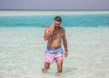 Yakışıklı adam Hint Okyanusu koyu mavi sudan gelen ve y telefon konuşma