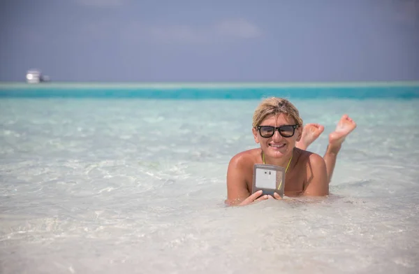 Vackra leende flicka lägger i blå vatten i Indiska oceanen med telefon — Stockfoto