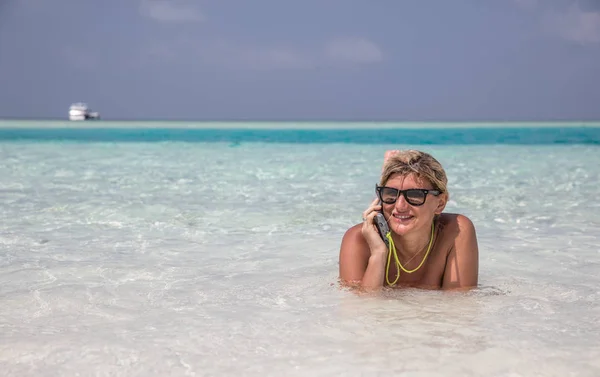 Mädchen liegt im blauen Wasser des Indischen Ozeans und telefoniert — Stockfoto