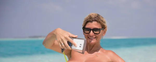 Vackra leende flicka gör selfie på stranden — Stockfoto