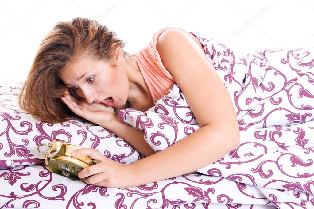 Woman in bed realizing that she has slept in despite having an alarm clock.