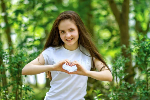 Mujer atractiva hace forma de corazón con sus manos en el bosque — Foto de Stock