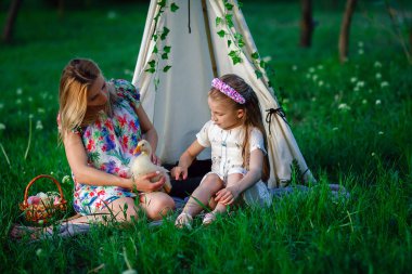 Anne ve kızı ile kaz oynarken çimenlerin üzerinde oturan