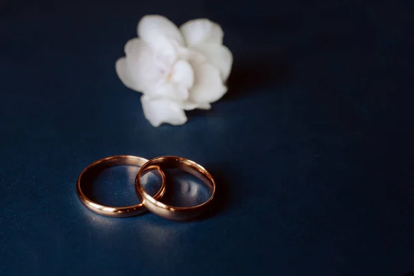 白の花と青の背景に結婚指輪をぼかす 低キーショット — ストック写真