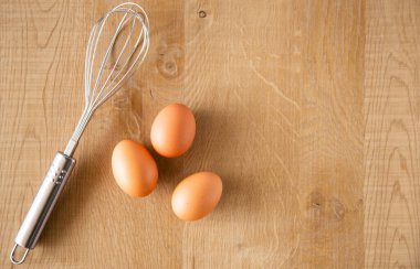 Tahta arka planda tavuk yumurtası ve yumurta çırpıcısı..