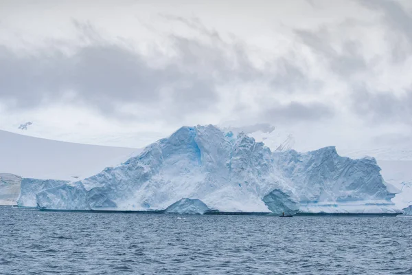 Hombre en un pequeño bote de goma junto a iceberg flotando en el océano. Península Antártica — Foto de Stock