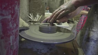 Öğretmen çömlekçi çarkındaki kille çocuğun çalışmasına yardım eder..