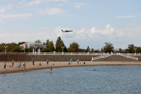 La gente en la playa de arena mira el avión volador — Foto de Stock