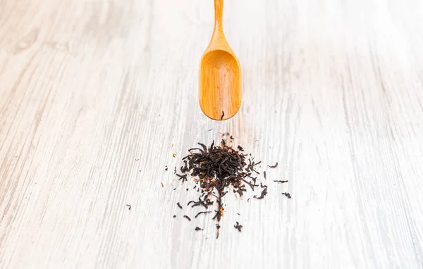 Composition of natural black tea with a leaves of rose. Macro photo of tea petals on a wooden spoon with a rose. Tea with the ingredients of flowers and tea located on a wooden Board.