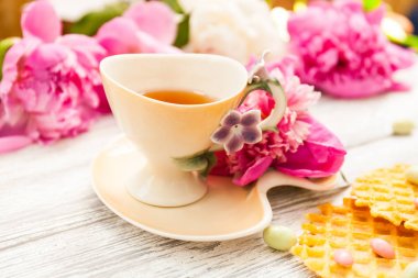 Fincan yeşil çay ve bahar peonies çiçeği waffle ve karamel eski bir ahşap zemin üzerine. Rustik.