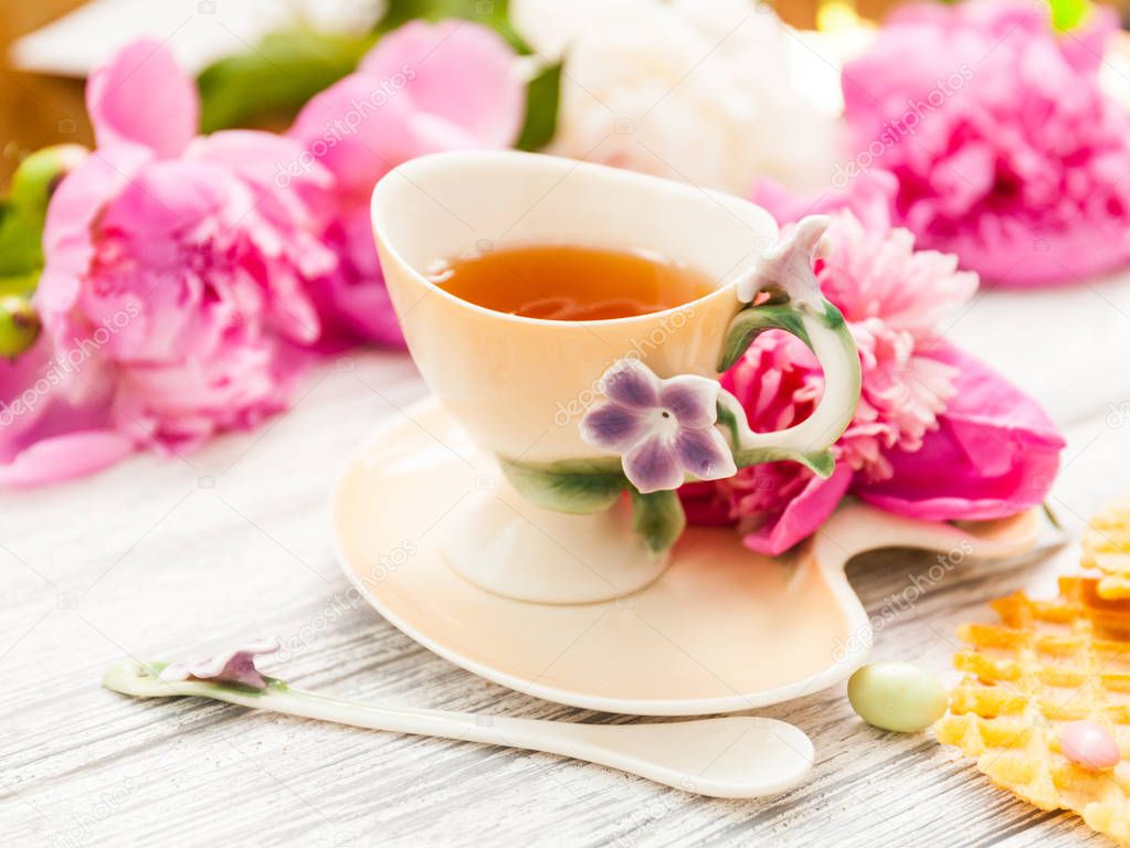 Cup of green tea and spring peonies blossom on a old wooden background with waffles and caramels. Rustic.
