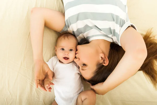 Szczęśliwa matka całuje dziecko leżące na łóżku — Zdjęcie stockowe