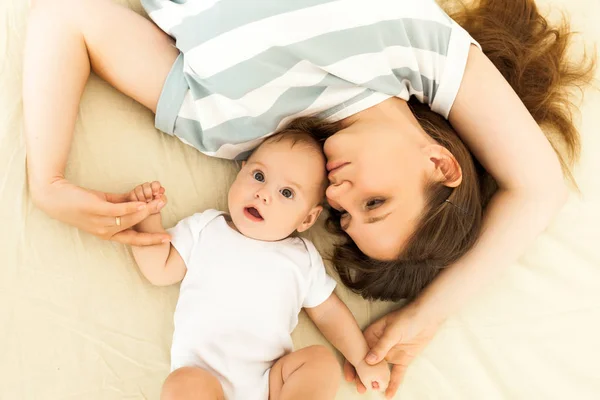 Happy mother kissing a baby lying on a bed — Stock Photo, Image