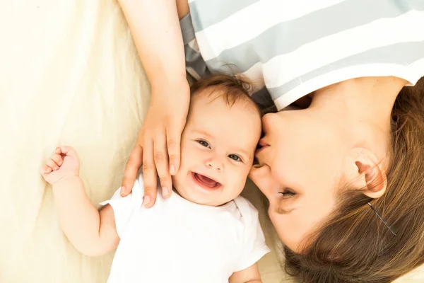 Mère heureuse embrassant un bébé couché sur un lit — Photo