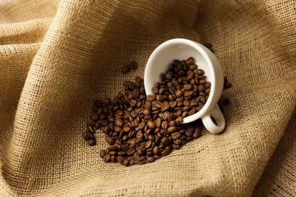 バラップにコーヒー豆を散らした白いカップ カップでコーヒー豆の散乱 粗い生地 — ストック写真