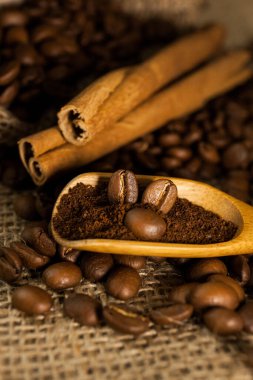 Yakın plan, ahşap kepçe kahve ve kahve çekirdekli tarçın çubukları çuval desenli arka plan.