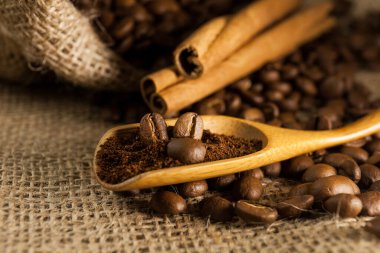 Yakın plan, ahşap kepçe kahve ve kahve çekirdekli tarçın çubukları çuval desenli arka plan.