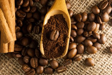 Yakın plan, ahşap kepçe kahve ve kahve çekirdekli tarçın çubukları çuval desenli arka plan.