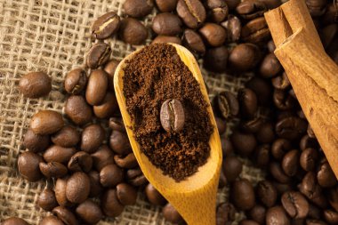 Yakın plan, ahşap kepçe kahve ve kahve çekirdekli tarçın çubukları çuval desenli arka plan.