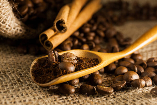 Close-up, wooden scoop with ground coffee and coffee beans, cinnamon sticks on a burlap textured background