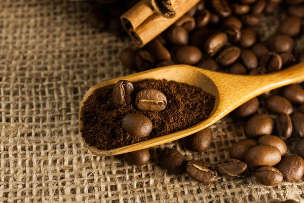 Close-up, wooden scoop with ground coffee and coffee beans, cinnamon sticks on a burlap textured background