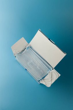 Cerrahi koruyucu maske. Tıbbi solunum bandajı kutusu mavi arka planda maske sıkıntısı çekiyor. Virüs ve salgın COVID-19 'un yayılmasının önlenmesi.