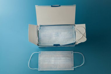 Cerrahi koruyucu maske. Tıbbi solunum bandajı kutusu mavi arka planda maske sıkıntısı çekiyor. Virüs ve salgın COVID-19 'un yayılmasının önlenmesi.