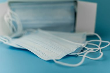 Cerrahi koruyucu maske. Tıbbi solunum bandajı kutusu mavi arka planda maske sıkıntısı çekiyor. Virüs ve salgın COVID-19 'un yayılmasının önlenmesi.