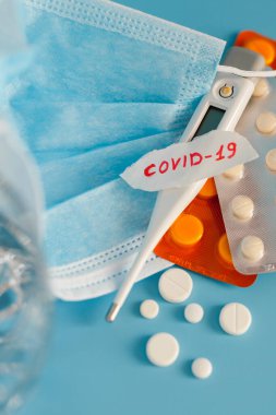 2019 nCoV adlı roman Coronavirus hastalığı. Kağıt üzerinde solunum maskesi, termometre ve haplarla birlikte el yazısı. Mavi arka plan üzerine seçici bir odaklanma.