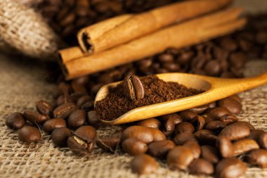 Yakın plan, ahşap kepçe kahve ve kahve çekirdekli tarçın çubukları çuval desenli arka plan.