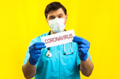 Koronavirüs karantinası kavramı. Roman Coronavirus 2019 NCoV. Sarı Arkaplan 'a karşı steteskoplu bir doktor elinde Coronavirus yazan beyaz bir kağıt tutuyor..
