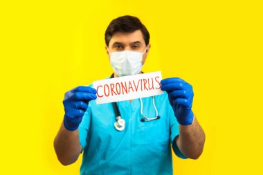 Koronavirüs karantinası kavramı. Roman Coronavirus 2019 NCoV. Sarı Arkaplan 'a karşı steteskoplu bir doktor elinde Coronavirus yazan beyaz bir kağıt tutuyor..
