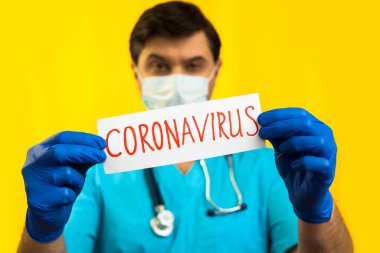 Koronavirüs karantinası kavramı. Roman Coronavirus 2019 NCoV. Sarı Arkaplan 'a karşı steteskoplu bir doktor elinde Coronavirus yazan beyaz bir kağıt tutuyor..