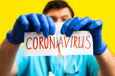 Koronavirüs karantinası kavramı. Roman Coronavirus 2019 NCoV. Sarı zemin üzerinde steteskopu olan doktor beyaz kağıdı Coronavirus sözcüğüyle yırt.