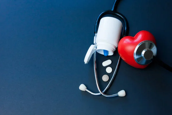 赤いおもちゃの心臓 錠剤の瓶と濃い青の聴診器 心臓病の予防と心血管疾患の概念 — ストック写真