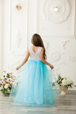 Küçük güzel ve şirin bir kız çocuğu. Şenlikli, açık mavi bir elbise içinde iç mekânda.
