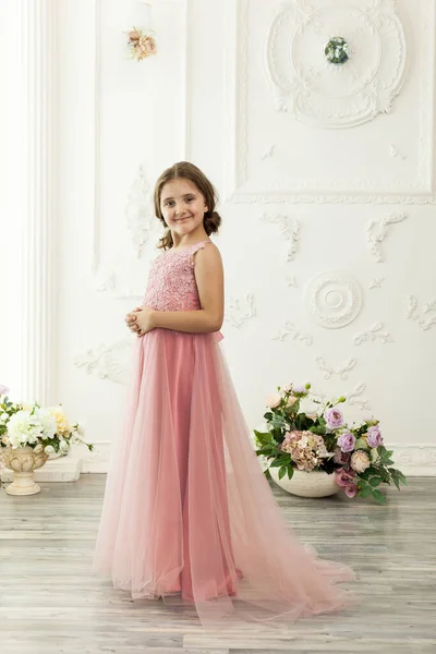 Little beautiful and cute girl child in a fashionable festive powdery pink dress in a interior